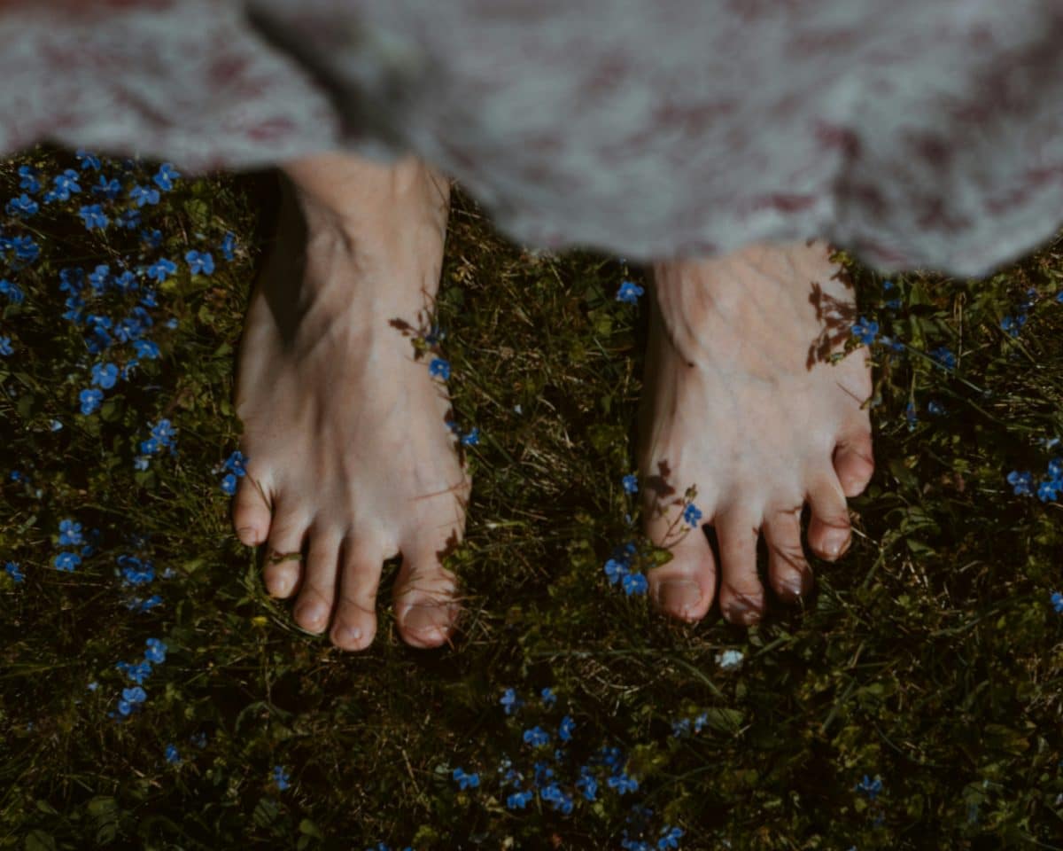 Pieds nus posés sur de l’herbe avec de petites fleurs bleues