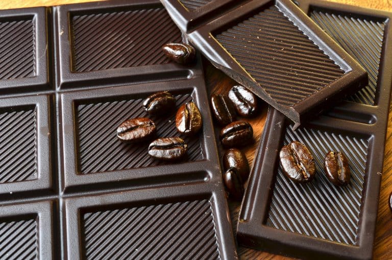 Carrés de chocolat noir disposés sur une table en bois, avec quelques grains de café posés sur les tablettes.