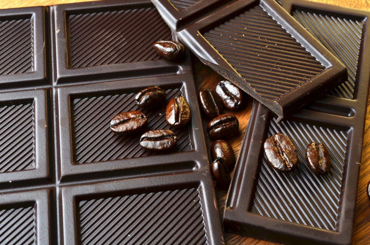 Carrés de chocolat noir disposés sur une table en bois, avec quelques grains de café posés sur les tablettes.