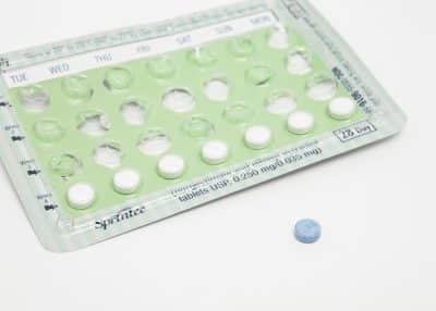 Plaquette de pilule contraceptive Sprintec avec plusieurs comprimés blancs et une pilule bleue posée à côté.